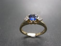 This brilliant three-stone engagement ring is set in 14K White / yellow gold. The center stone, a 5mm round brilliant cut natural blue sapphire is set in a four prong setting and adorned by two round brilliant cut diamonds with total carat weight of 0.20cttw. Diamonds Quality: D-F in Color and VS in Clarity with Heart and Arrow (Ideal cut) Currently made to order pieces may take up to 10-15 business days to complete, or let me know if you need it urgent. You may also like: A similar diamond and Wedding Sapphire Three-stone Jewelry, Sapphire Three Stone Jewelry For Wedding, Three Stone Sapphire Jewelry For Wedding, Yellow Gold Three Stone Sapphire Wedding Ring, White Gold Three Stone Sapphire Wedding Ring, Elegant Three Stone Sapphire Ring For Wedding, Elegant Three-stone Sapphire Ring For Wedding, Timeless Blue Wedding Dress, Blue Diamond Three Stone Wedding Ring