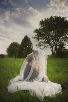 a bride and groom sitting in the grass under a veil