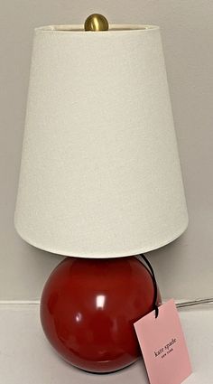 a red table lamp sitting on top of a white floor next to a pink tag