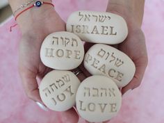 four white stones with words written on them in different languages are held by a woman's hands