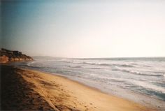 a sandy beach next to the ocean with waves coming in from the shore and people walking on the sand