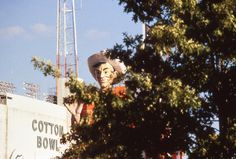 a large statue of a man wearing a cowboy hat in front of a cotton bowl sign