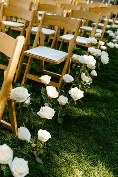 rows of wooden chairs with white flowers on the grass in front of them at an outdoor ceremony