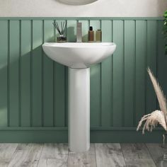 a white pedestal sink in a bathroom with green walls and wood flooring next to a round mirror