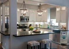 a kitchen with white cabinets and black counter tops, lights hanging from the ceiling over the island