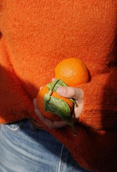 a person is holding an orange in their left hand while wearing a sweater and jeans