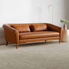 a brown leather couch sitting on top of a carpeted floor next to a lamp