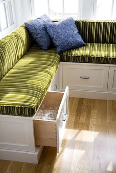 a green and white striped couch with drawers underneath it in a room that has wood floors