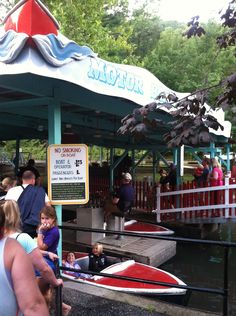 people are standing near a boat in the water at an amusement park with a sign on it