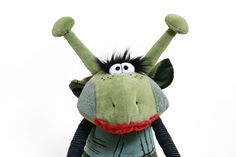 a green stuffed animal with black hair and big eyes on it's face, arms and legs