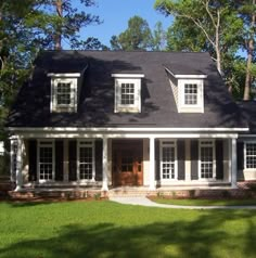 a white house with black shingles and two windows on the front porch, surrounded by trees