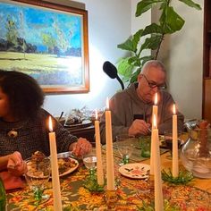 people sitting at a table with candles in front of them and plates on the table