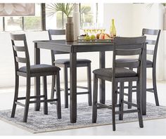 a dining room table with four chairs and a tray of fruit on the counter top