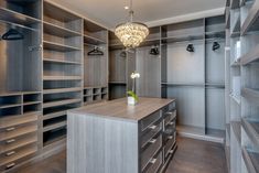 a large walk in closet with lots of shelves and drawers on each side, along with a chandelier hanging from the ceiling