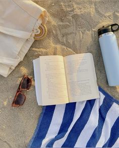 an open book and sunglasses on the beach next to a water bottle, towel, and sunshade