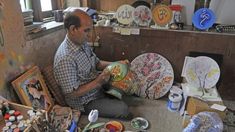 a man sitting on the floor in front of some paintings and other art supplies,