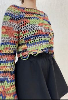 a woman wearing a multicolored sweater and black skirt with her hands in her pockets