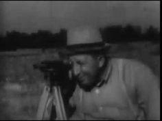 black and white photograph of a man with a camera on tripod looking at something in the distance