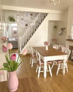 a dining room table and chairs with pink flowers in a vase on the floor next to stairs