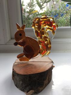 a glass squirrel figurine sitting on top of a piece of wood next to a window