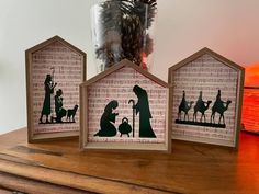 three nativity scene silhouettes are displayed on a wooden table next to a vase filled with pine cones