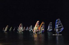 a group of sailboats sailing in the ocean at night with bright lights on them