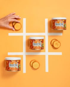 three cans of tea and four cookies on an orange surface with white squares in the middle