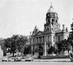 an old black and white photo of cars parked in front of a large building with a steeple