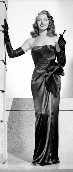 an old black and white photo of a woman in a long dress with gloves on