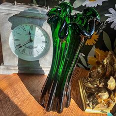 a green glass vase sitting on top of a wooden table next to a small clock