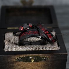 two black rings with red flowers on them sitting in a wooden box next to each other