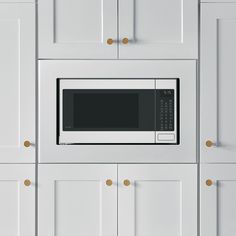 a microwave built into the side of a white kitchen cabinet with gold knobs on it