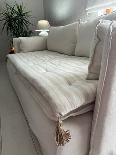 a bed with white linens and pillows on it, next to a potted plant