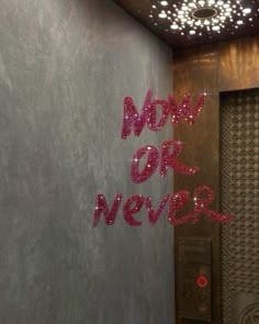 the words now or never are spelled with pink sparkles in front of a gray wall