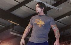 a man with long hair and tattoos on his arm is skateboarding in a parking garage