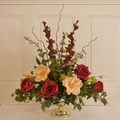 a vase filled with red and yellow flowers on top of a white table next to a wall