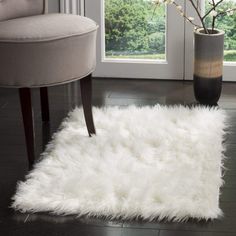 a white area rug on the floor next to a chair and vase with flowers in it