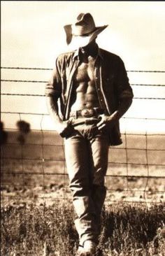 a shirtless man wearing a cowboy hat standing in front of a fence