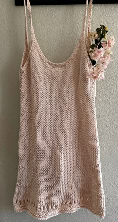 a crocheted tank top hanging on a wall with flowers in the bottom right corner