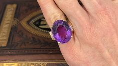 This amethyst cocktail ring is centered with one (1) oval mixed cut natural amethyst set into a four-prong setting. The shoulders of the ring are each accented with five (5), bead set, round brilliant cut diamonds. The ring measures 20.0mm at the top, rises 12.1mm above the finger, tapering to 3.3mm wide and 0.9mm thick at the base of the shank. The ring is currently a size 5. Oval Amethyst Ring With Gemstone Accents For Formal Occasions, Oval Amethyst Ring For Formal Occasions, Oval Amethyst Gemstones For Formal Occasions, Formal Oval Amethyst Gemstones, Luxury Purple Amethyst Oval Cabochon Ring, Oval Amethyst Ring With Gemstone Accents, Oval Purple Amethyst Ring With Gemstone Accents, Luxury Purple Oval Gemstones, Heirloom Style Purple Oval Amethyst Ring