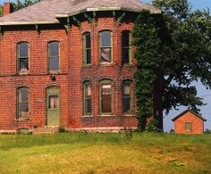 an old red brick house sitting on top of a lush green field