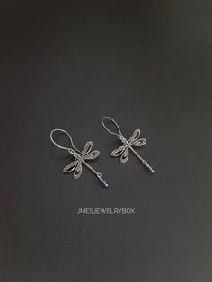 two silver dragonfly earrings on a black background