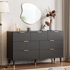 a black dresser with gold handles and drawers in front of a large round mirror on the wall