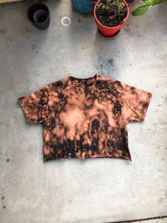 a brown and black tie dye shirt sitting on top of a cement floor next to potted plants