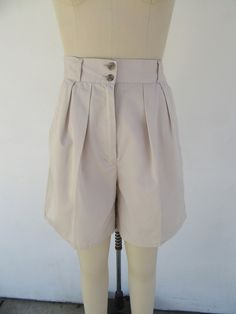 80s or maybe 90s high waist pleated khaki shorts. 65/35 poly cotton blend. Four pockets. Button detail on back. Super cute. Lightweight. Made  in Indonesia for 10 BROWING ST.  Label size 7/8 Please compare measurements to a similar garment that fits you well Measured flat 27" Waist 14" rise 40" hips 6-3/42" inseam   Good vintage condition with light signs of use and age. Classic Summer Shorts With Button Closure, Vintage Shorts With Button Closure For Summer, High Waist Vintage Shorts For Workwear, Vintage High Waist Shorts For Workwear, Vintage High-waist Shorts For Work, Vintage Workwear Shorts For Summer, Beige High-waisted Shorts With Button Closure, Classic High Waist Beige Shorts, Classic Beige High Waist Shorts