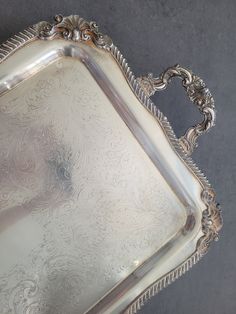 an antique silver tray with ornate designs on the handles and sides, set against a gray background