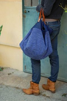 a person standing on the sidewalk with a blue handbag in their pocket and brown boots