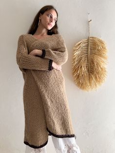 A person with long hair stands against a beige wall Long Beige Cozy Outerwear, Beige Long Cozy Outerwear, Beige Wool V-neck Outerwear, Oversized Long Beige Sweater Coat, Beige Knitted Wool Sweater Coat, Beige Wool Knitted Sweater Coat, Oversized Neutral Sweater Coat For Winter, Beige Wool Sweater Coat For Fall, Cozy Long Beige Cardigan