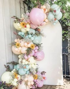 balloons and flowers are hanging from the side of a white wall in front of a gate