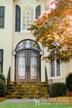 the front entrance to a large white house with black shutters and iron doors on it